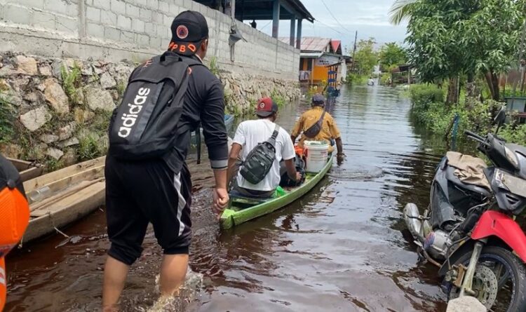 Petugas dari BPBD Palangka Raya tampak membantu warga yang melintas di daerah banjir menggunakan sampan (Ist)