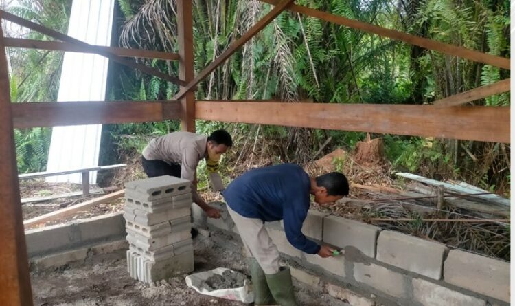 Teks Poto: Bhabinkamtibmas Kelurahan Marang, Polsek Bukit Batu, Aiptu Abdul Aziz, pada saat membantu pembangunan gudang alat dan posko karhutla.